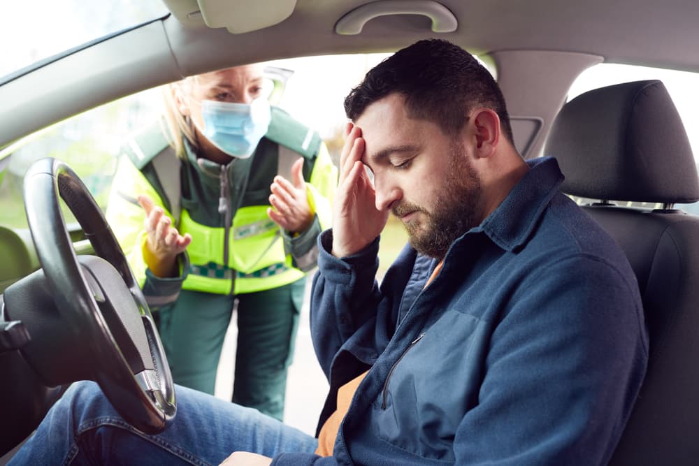 A female paramedic assisting a male driver with whiplash neck injury after a road traffic accident.