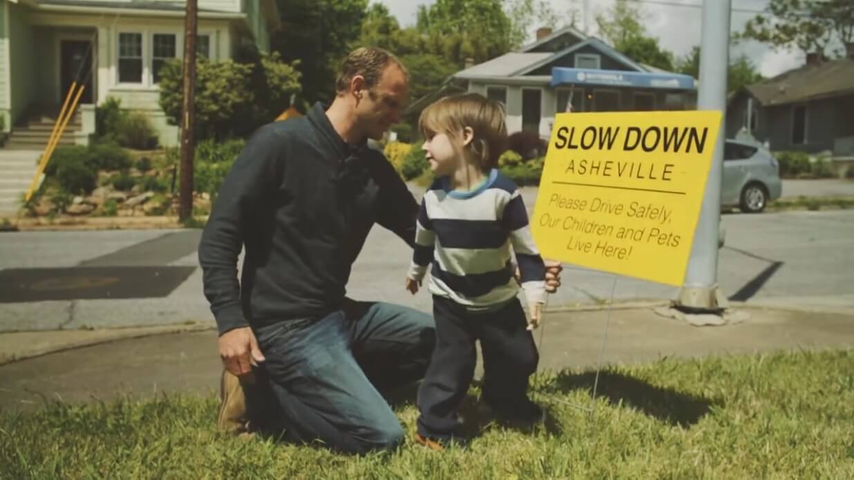 Lakota Denton with child holding Slow Down Asheville campaign sign