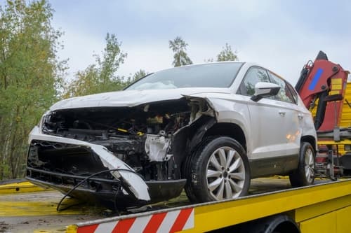 White SUV with left headlights and bumper section missing on bed of a tow truck