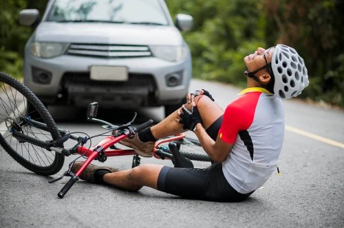 Bicyclist wearing shite shirt with red sleeves on ground holding knee wearing white bike helmet