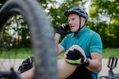 Man wearing bike helmet on floor holding knee while on photo with wheel rim in foreground